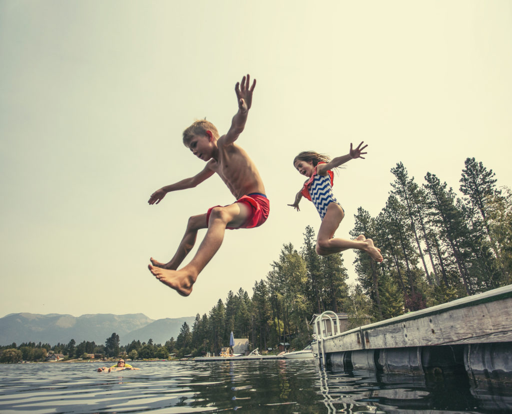 A little boy and little girl jumping off the dock into a beautiful mountain lake. Having fun on a summer vacation